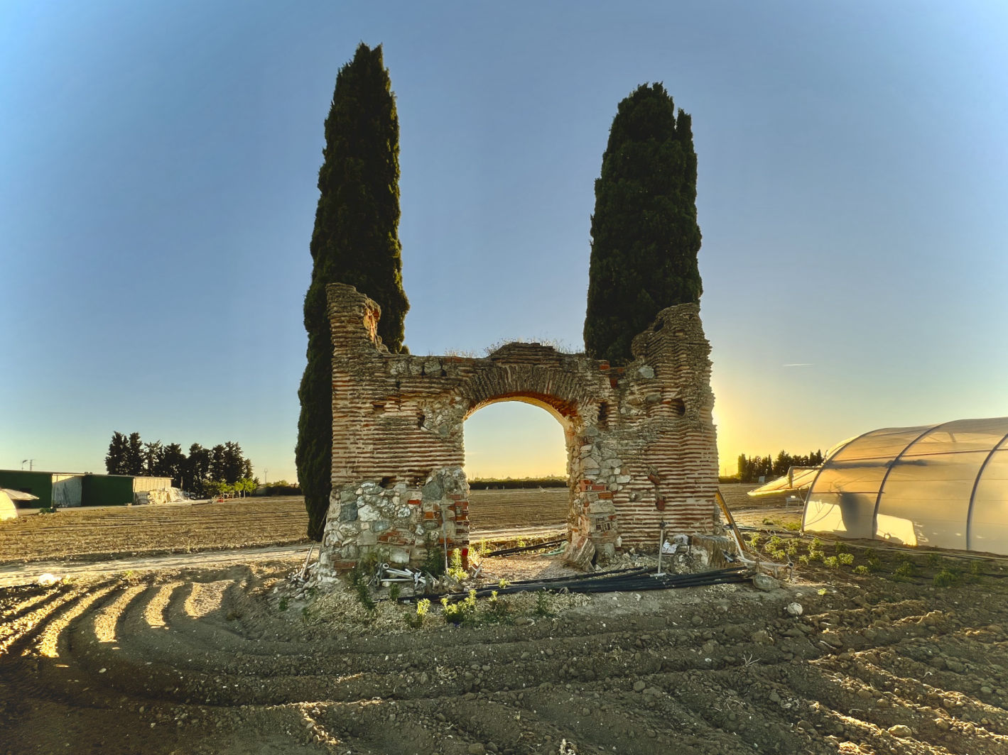 foto de los restos de la hermita antigua que danombre a la huerta el torreón con dos cipreses a cada lado y el sol de frente